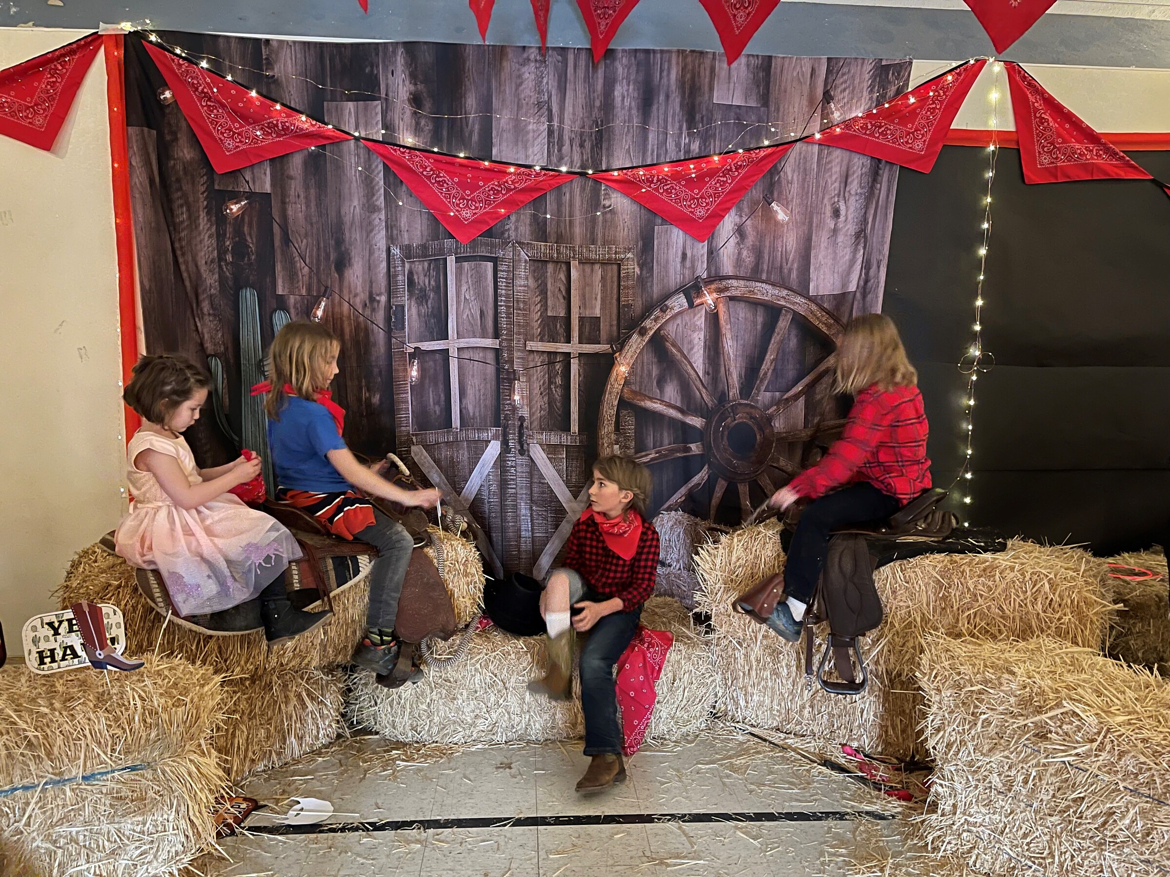 4 elementary students pose with hay bales, saddles, and a barn backdrop at the photobooth